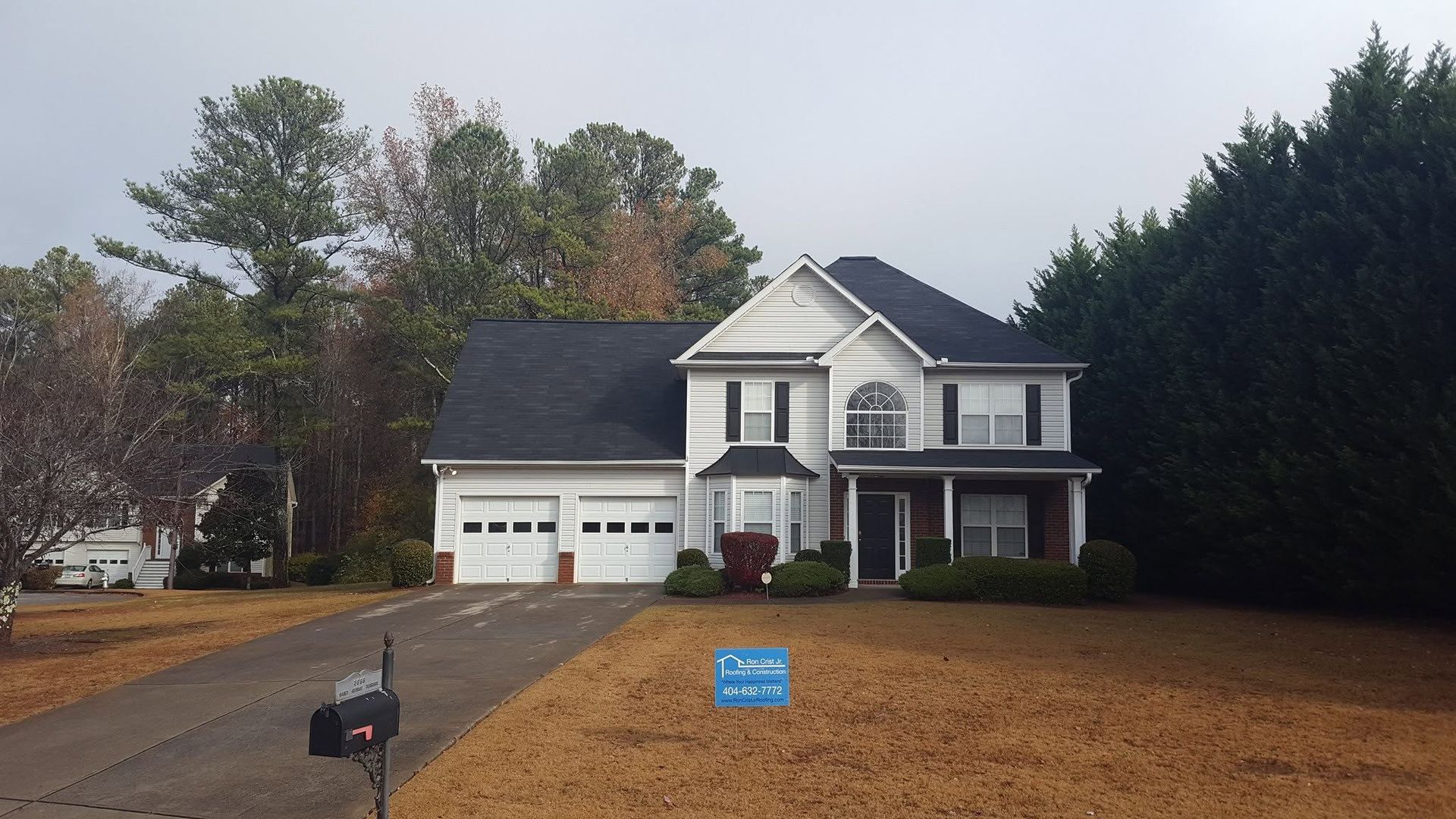 Suburban house with white siding, black roof, garage, and a small blue yard sign in front.
