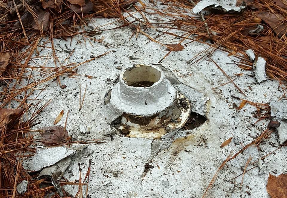 Broken white concrete pipe on a snow-dusted ground with pine needles and debris nearby
