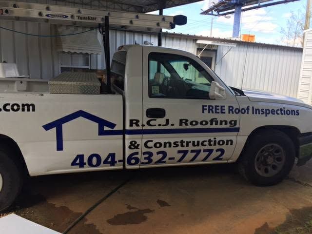 White R.C.J. Roofing & Construction truck parked under an awning, with “Free Roof Inspections” on the door