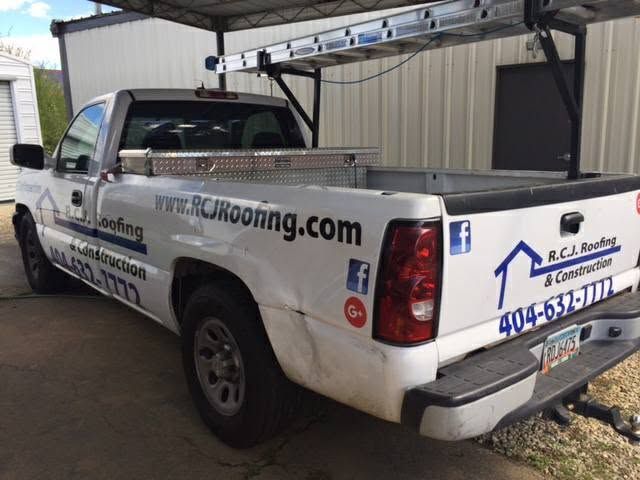White roofing pickup truck with company logos and ladder rack parked beside a building