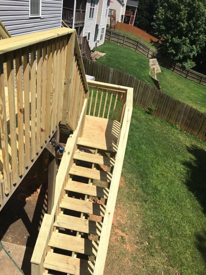 Wooden outdoor staircase with railings descending beside a house into a grassy backyard