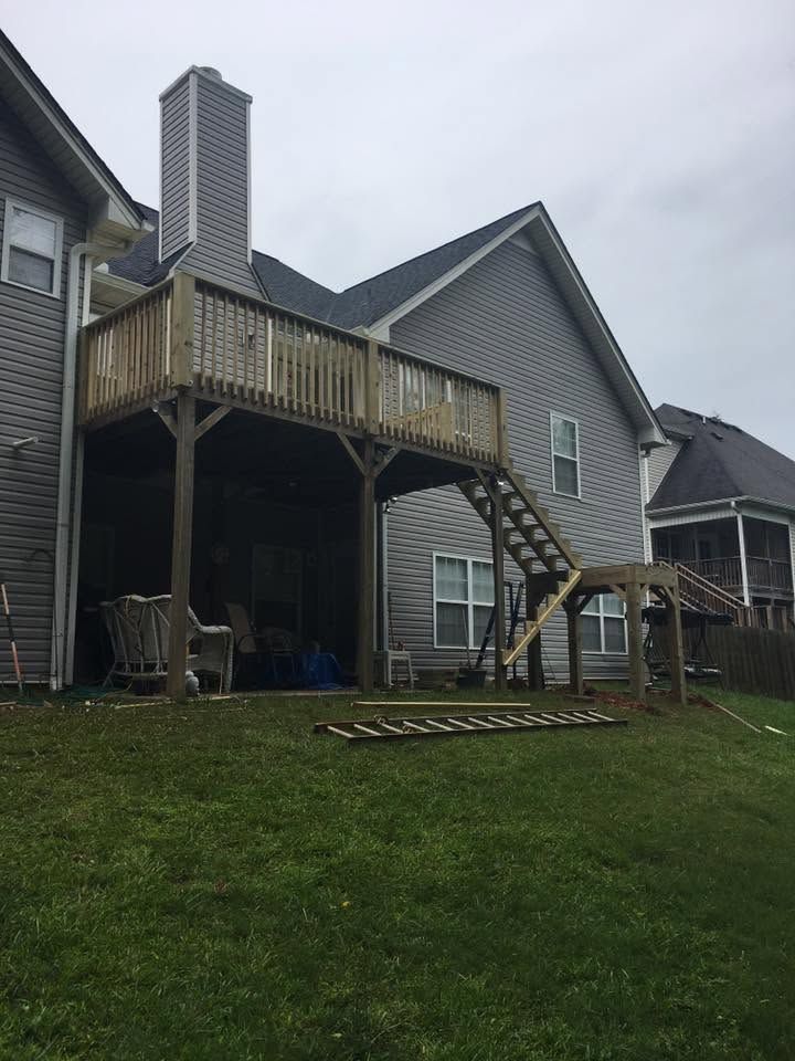 Backyard deck and stairs on a gray house, with a lawn and overcast sky.