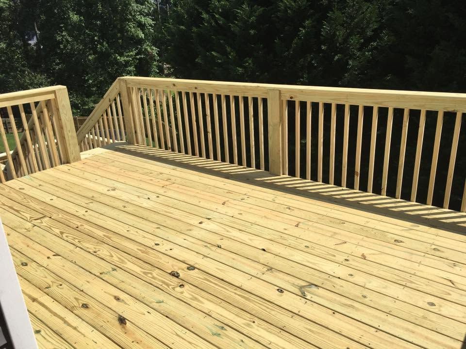 Wooden deck with railings overlooking a wooded area in bright sunlight