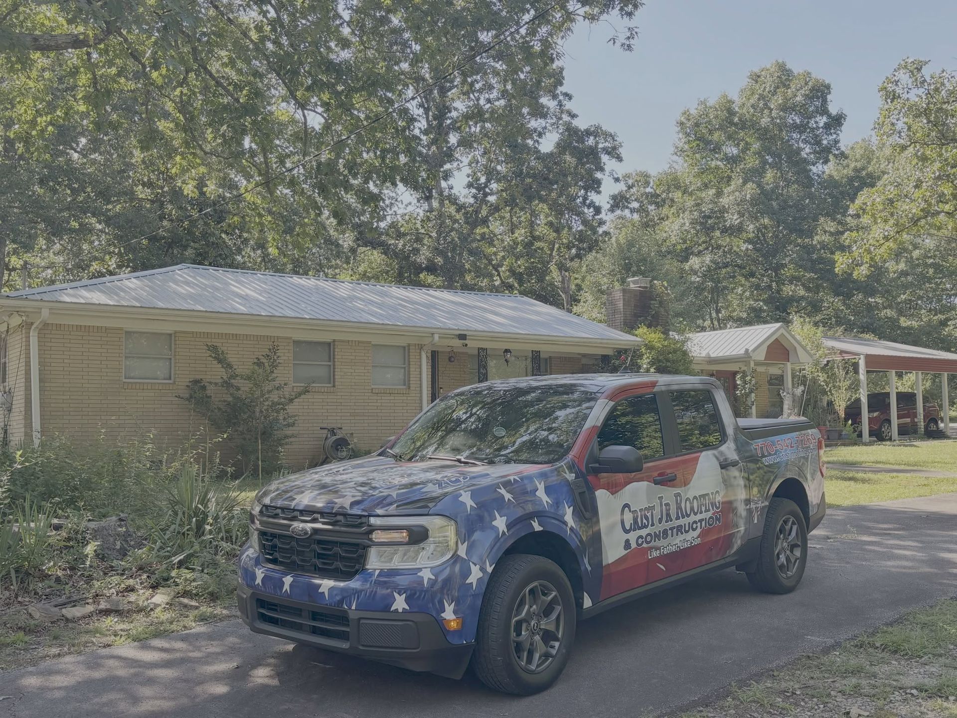 Branded blue pickup truck parked beside a house and tents in a leafy yard