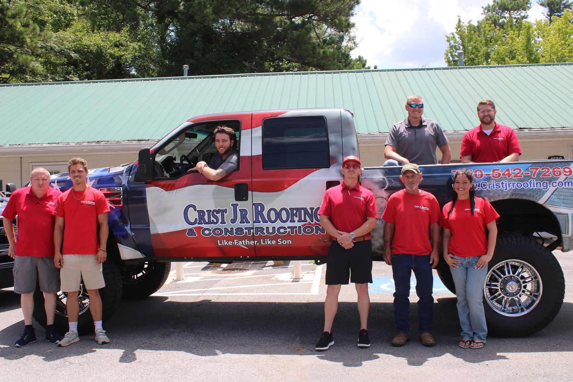 Group in red shirts posing beside a red, white, and blue lifted truck outdoors