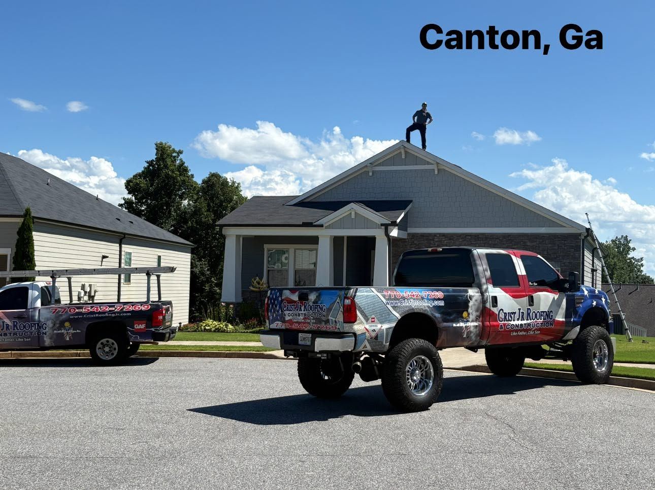Two lifted pickup trucks parked outside a house in Canton, Georgia, with a worker on the roof