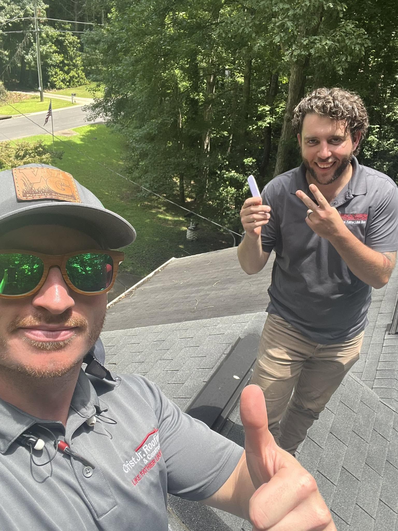 Two men outdoors on a sunny trail, smiling and posing with thumbs up and peace signs.