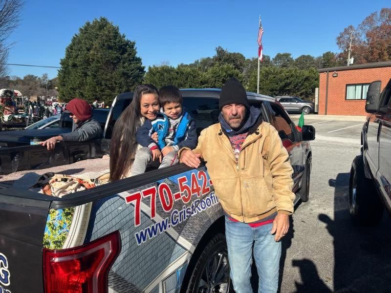 Family posing in the back of a decorated pickup truck on a sunny street with school building and flag nearby