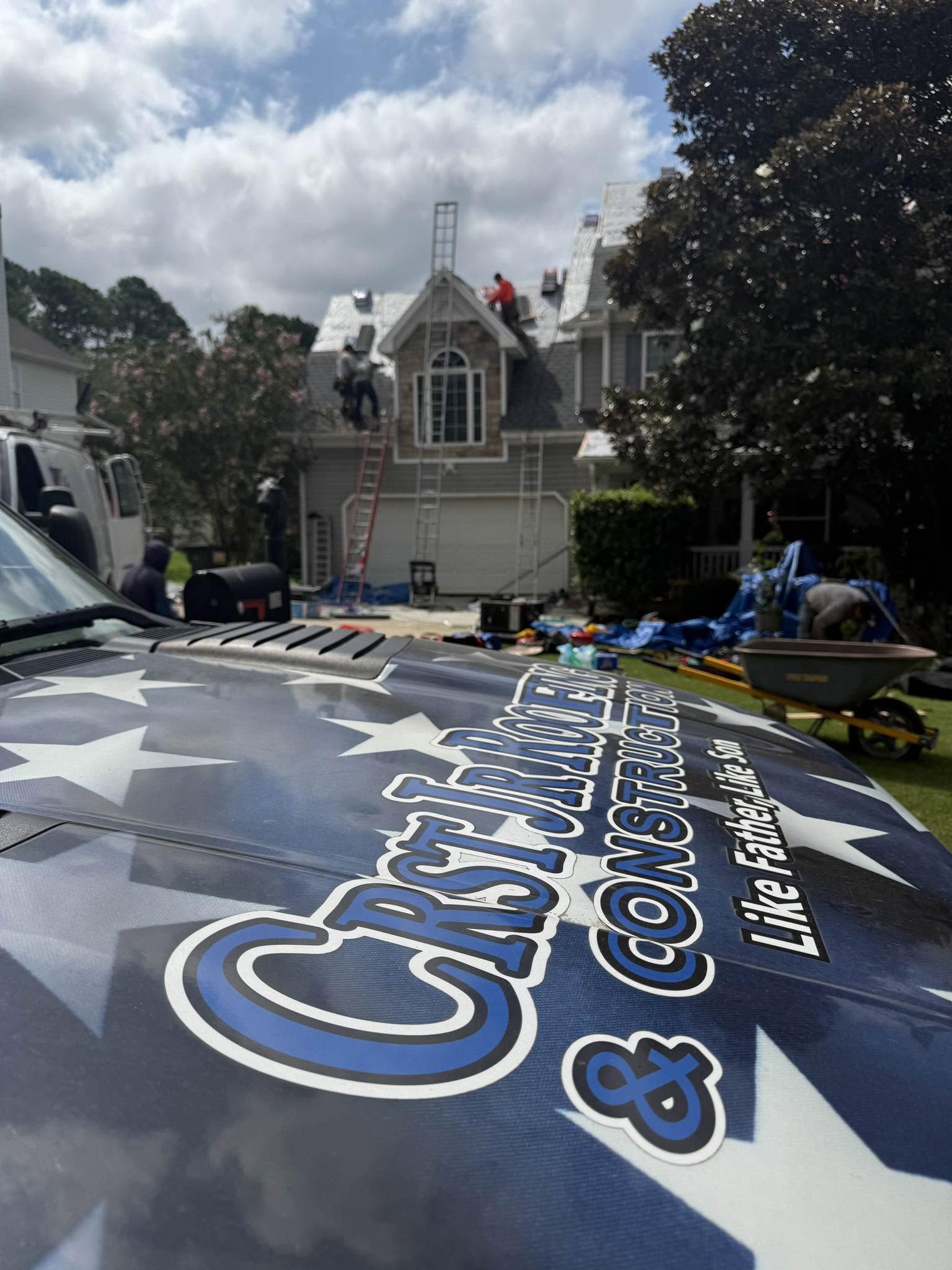 Large printed banner being laid out on a car in a driveway with a house in the background