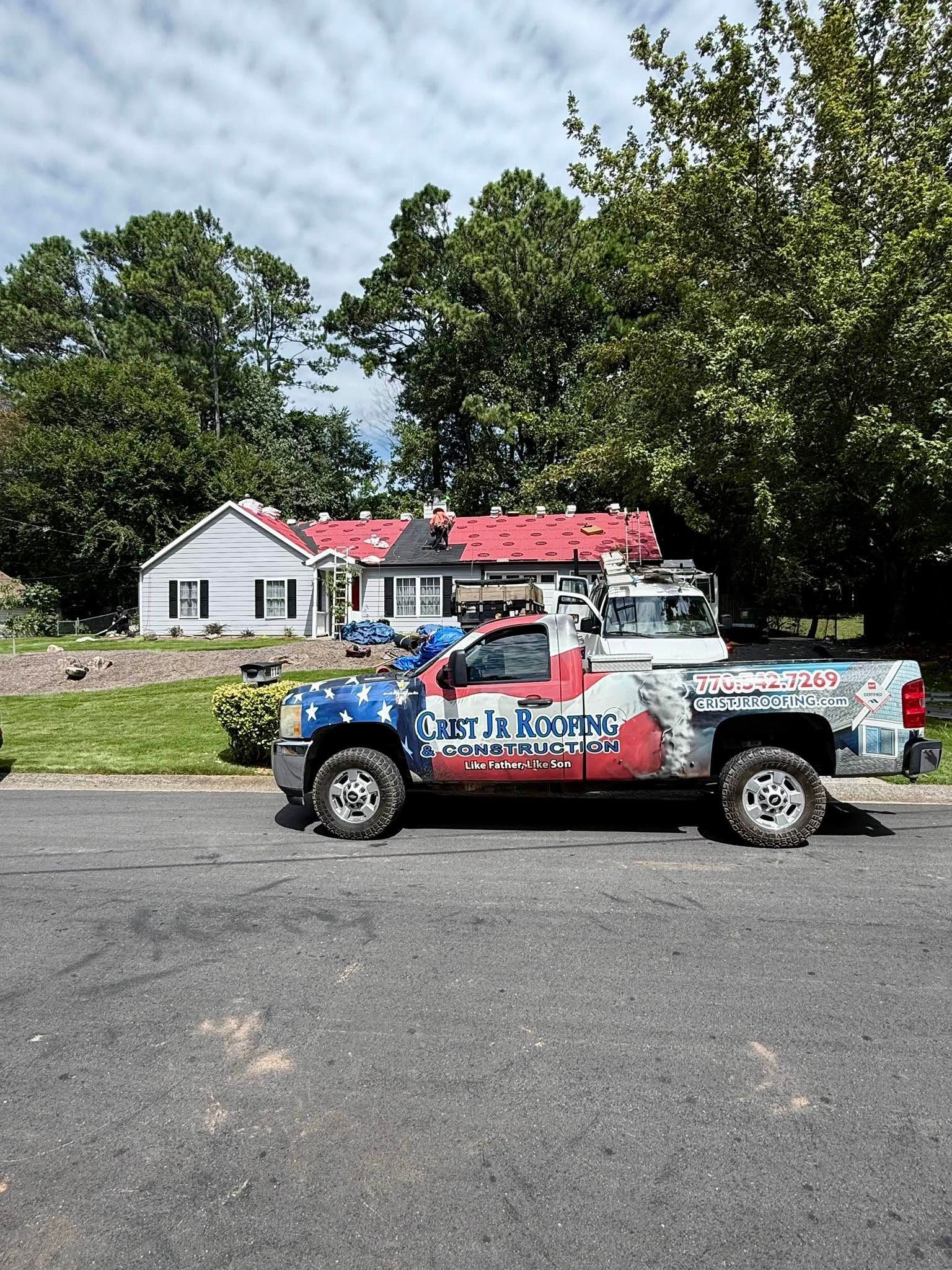 Blue-red service pickup truck parked on a gravel lot in front of a white house and trees