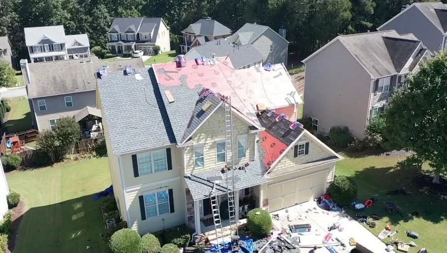 Aerial view of a house with storm-damaged roof and debris in a suburban neighborhood