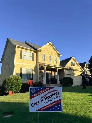 Yellow house with a roofing service yard sign on the lawn under a blue sky