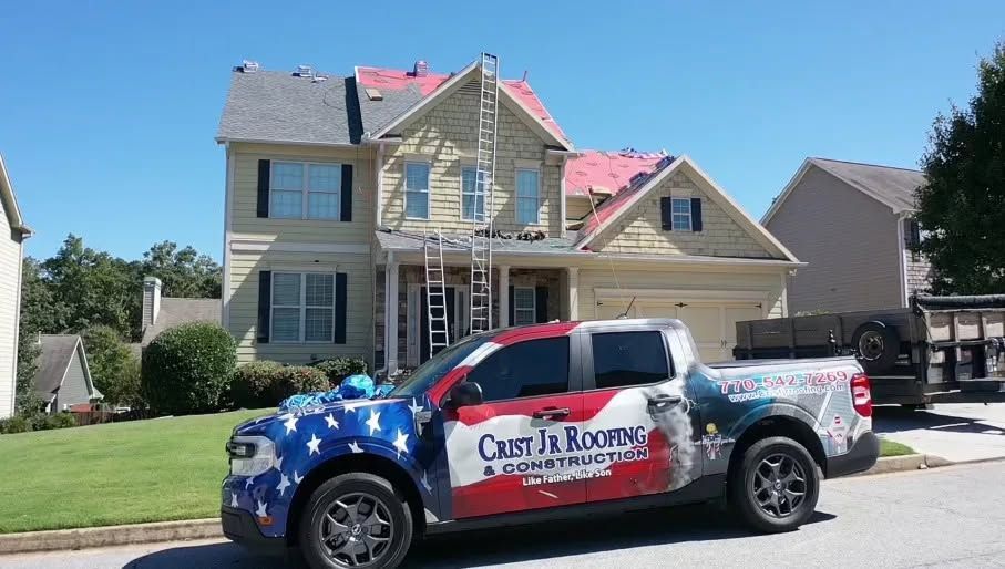 Branded service truck parked in front of a two-story house with a pink roof and blue sky.