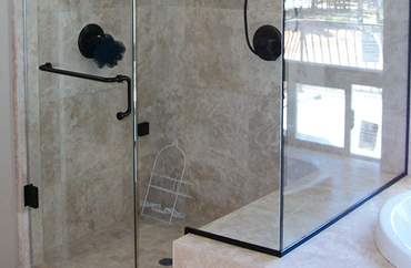 A glass shower enclosure with black hardware, stone-tiled walls, and a white shower caddy inside.