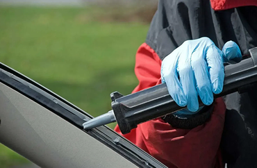 A gloved hand uses a black caulk gun to apply sealant along a seam on an exterior structure.