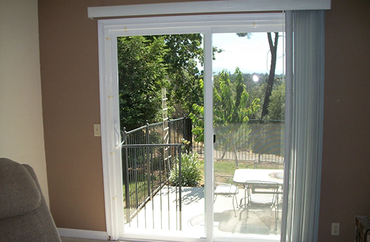 A glass sliding door opens onto a patio overlooking a fenced backyard with trees and a small white table.