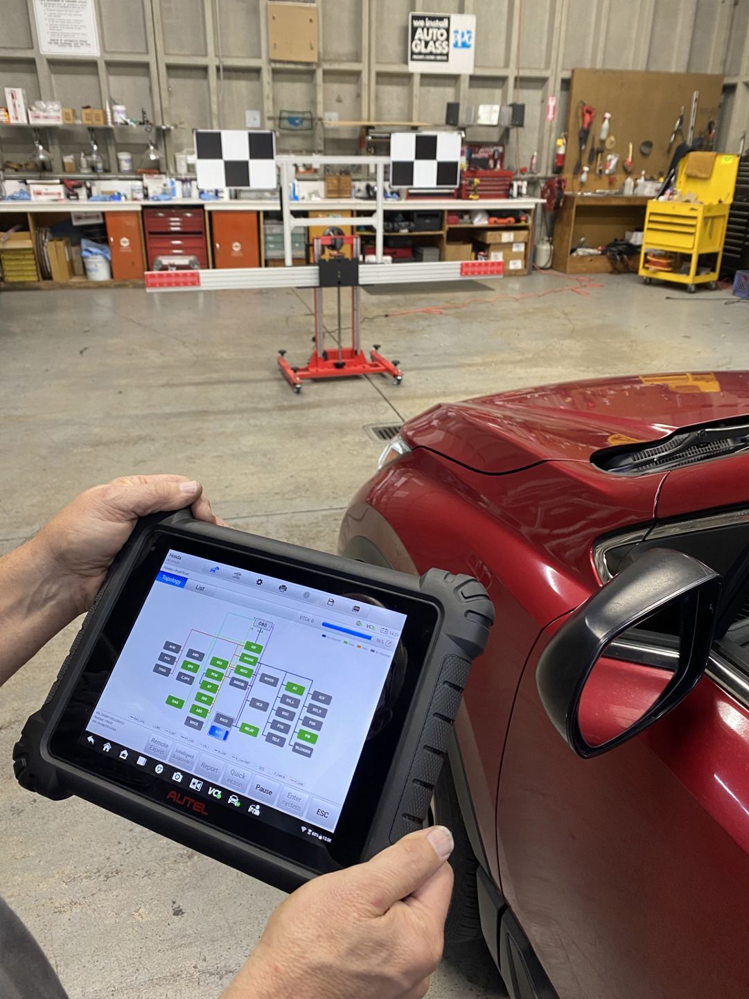 A person is holding a tablet in front of a red car in a garage.