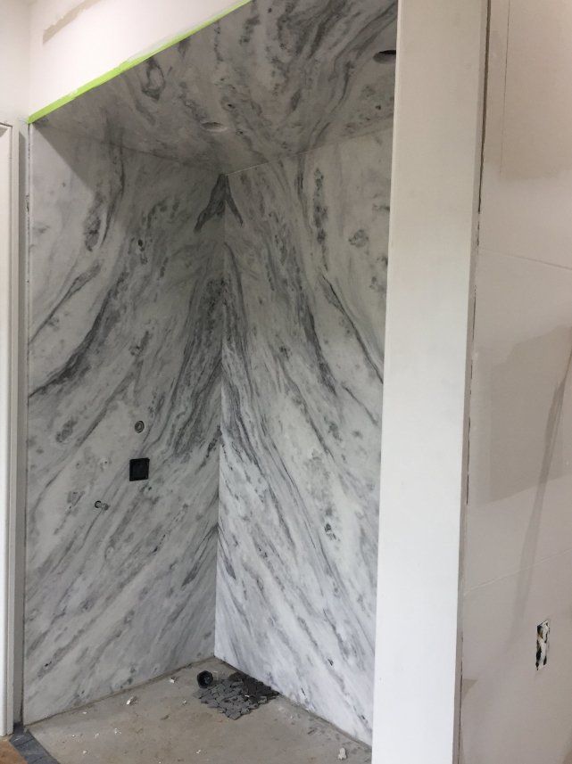 A bathroom with marble walls and a shower stall.