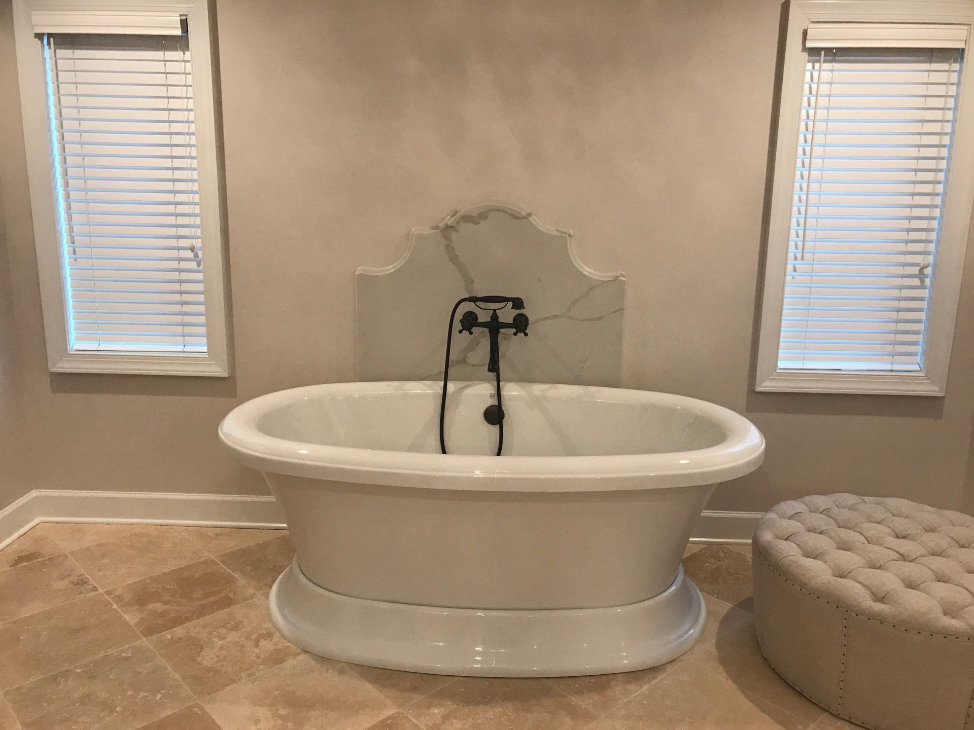 A white bathtub is sitting in a bathroom next to two windows.