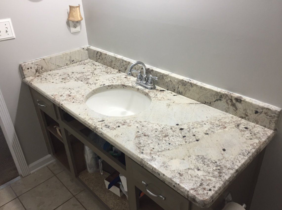 A bathroom sink with a granite counter top and a faucet.