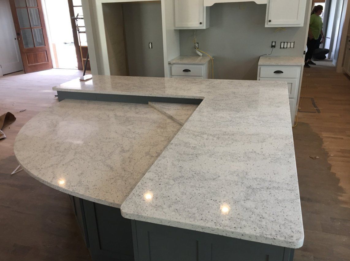 A kitchen with white granite counter tops and gray cabinets