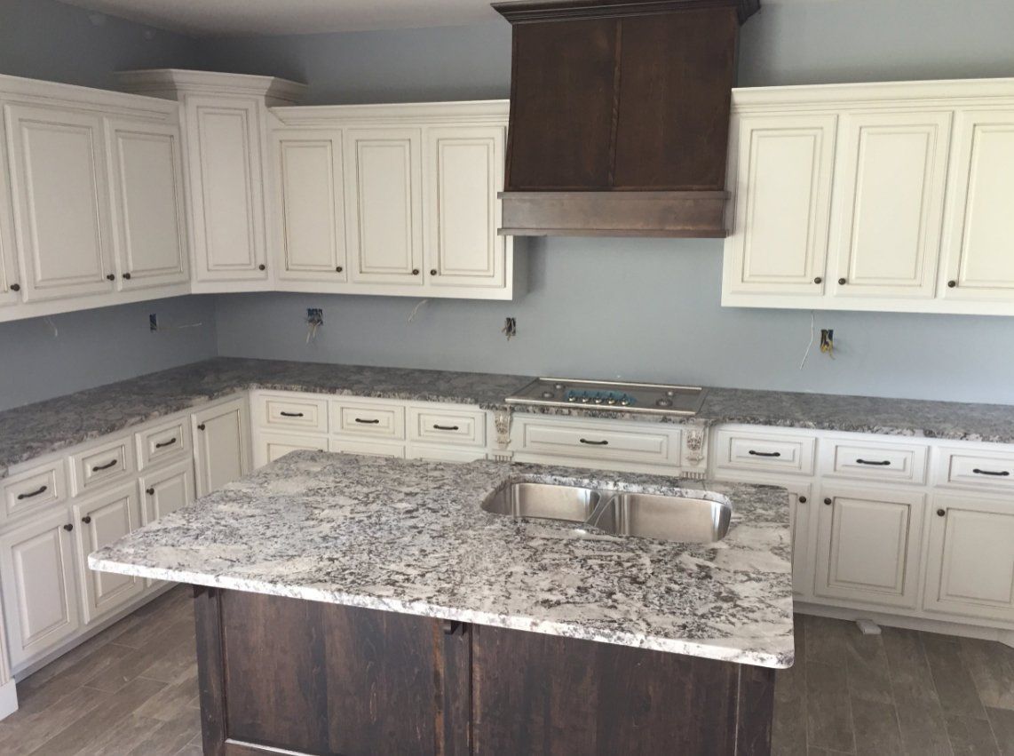 A kitchen with white cabinets and granite counter tops and a large island.