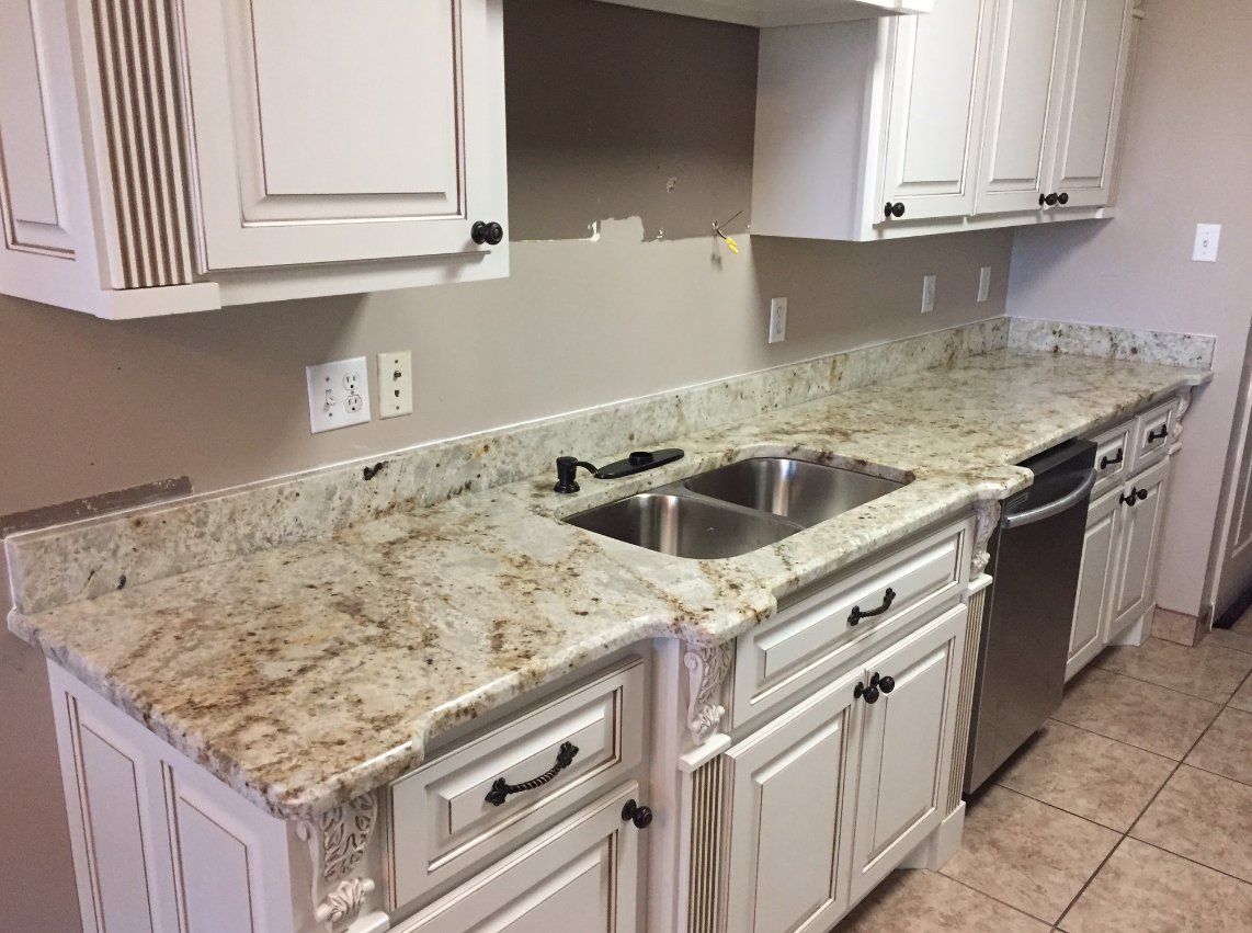 A kitchen with white cabinets , granite counter tops , a sink and a dishwasher.