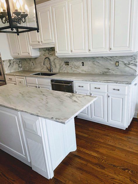 A kitchen with white cabinets and marble counter tops.