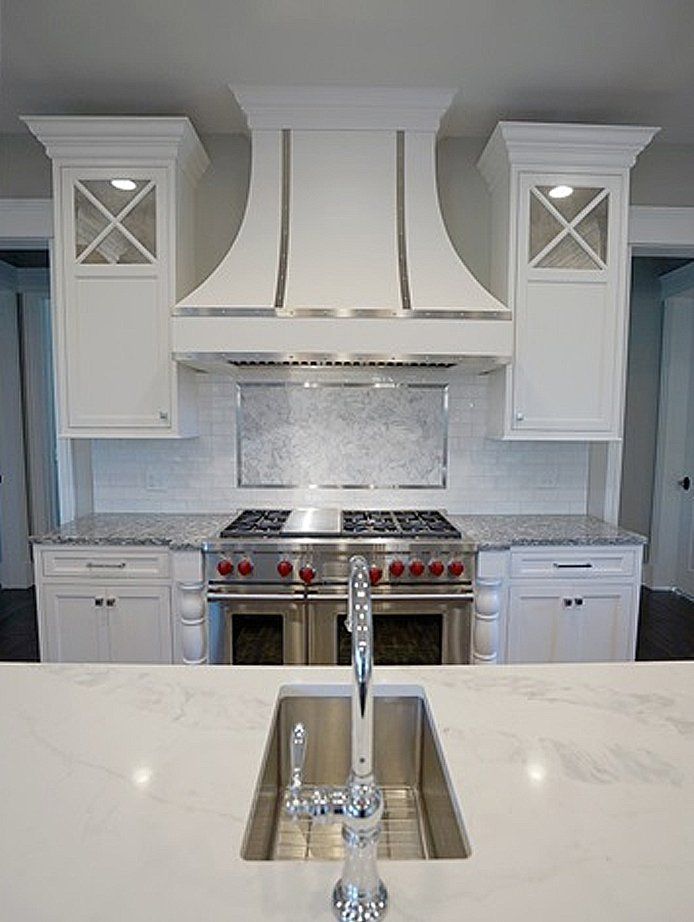 A kitchen with white cabinets , a stove , a sink , and a hood.