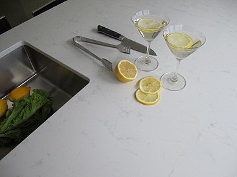 A kitchen counter with a sink , two martini glasses , lemons and tongs.