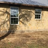 Stone building with two windows; shadows of a tree cast on the exterior.