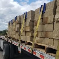 Truckload of stacked beige stone blocks, secured with straps. Cloudy sky in the background.