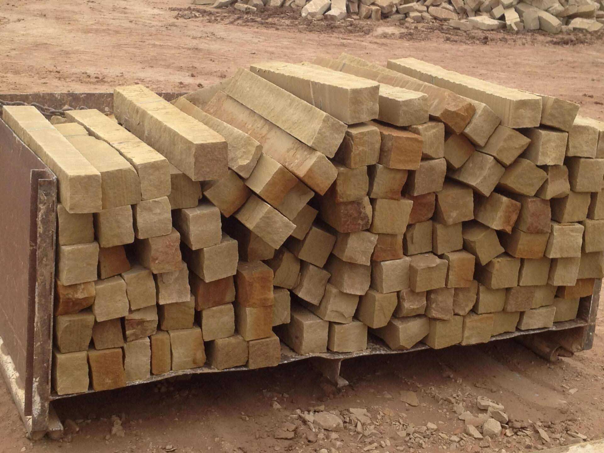 Pile of beige, square-cut sandstone blocks on a metal pallet, outdoors.