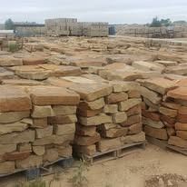 Stacks of brown and tan rectangular stones, likely for construction, outdoors on pallets.