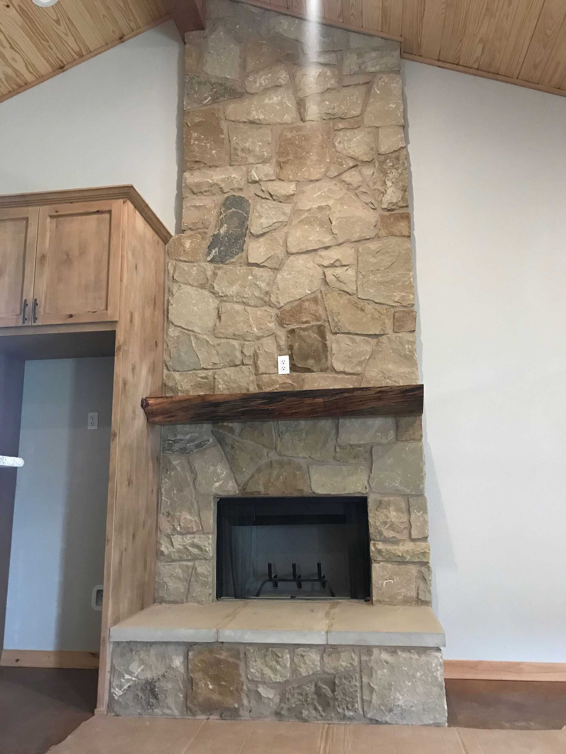 Stone fireplace with wooden mantel and cabinets, light-colored walls and ceiling.