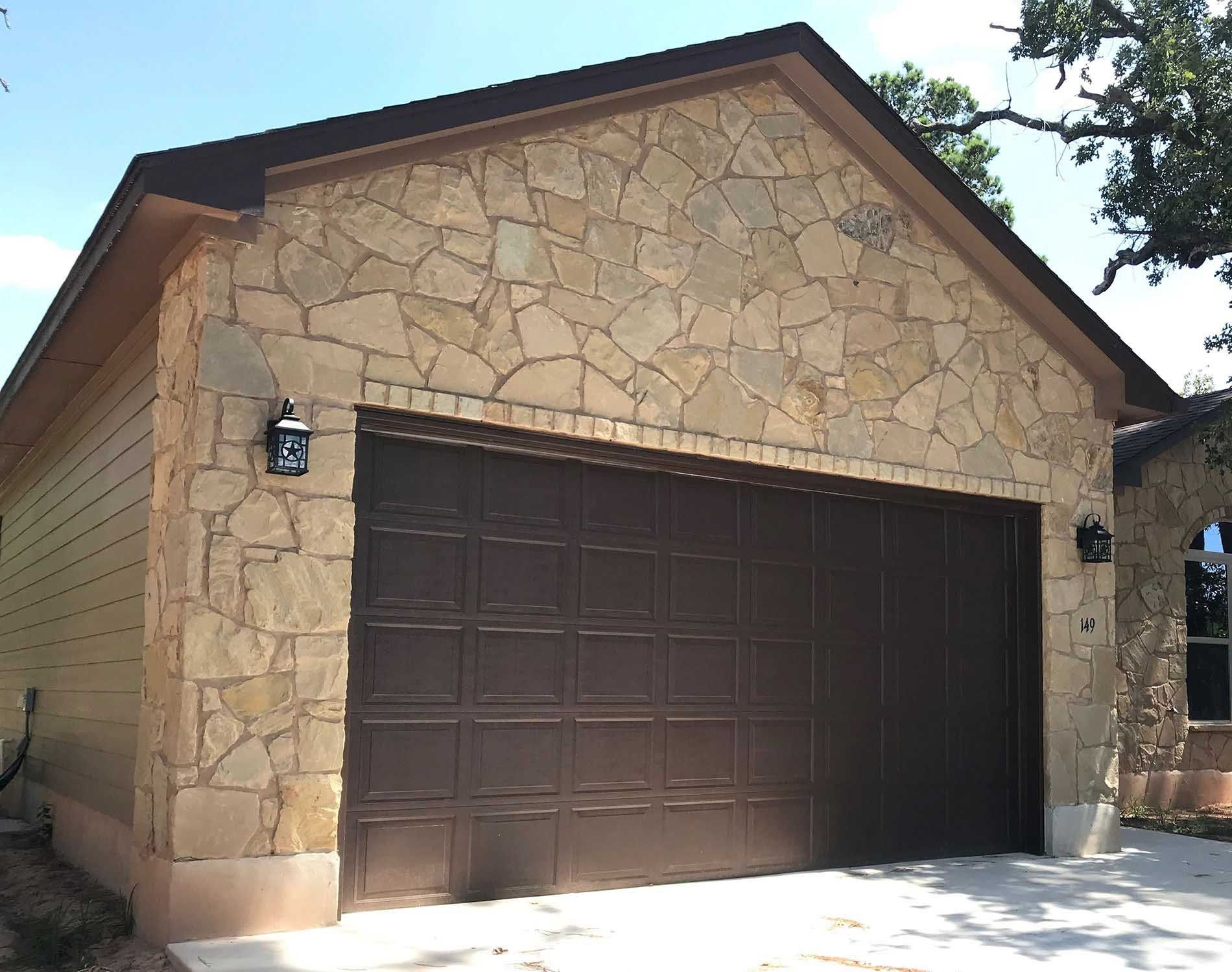Garage with brown door and stone facade, tan siding, and brown roof.
