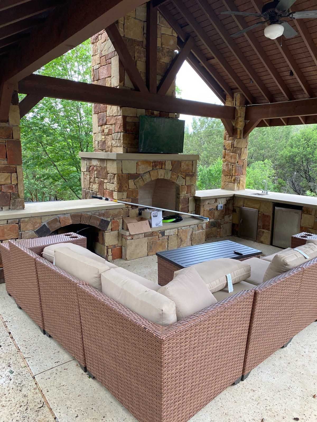 Outdoor stone-built patio with a fireplace, television, and wicker sectional seating.