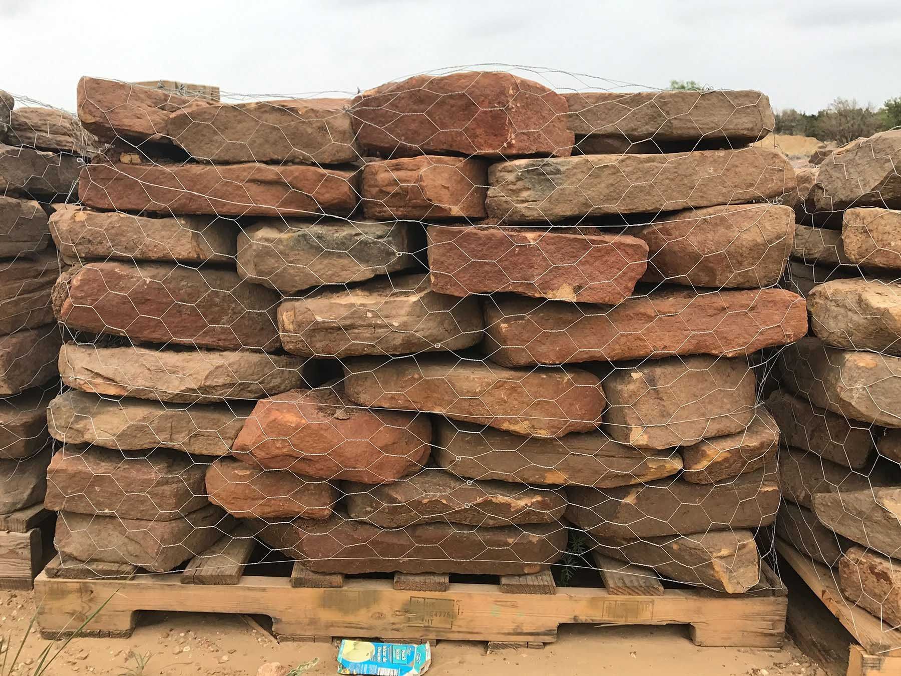 Stack of reddish-brown bricks, secured with netting, on a wooden pallet outdoors.
