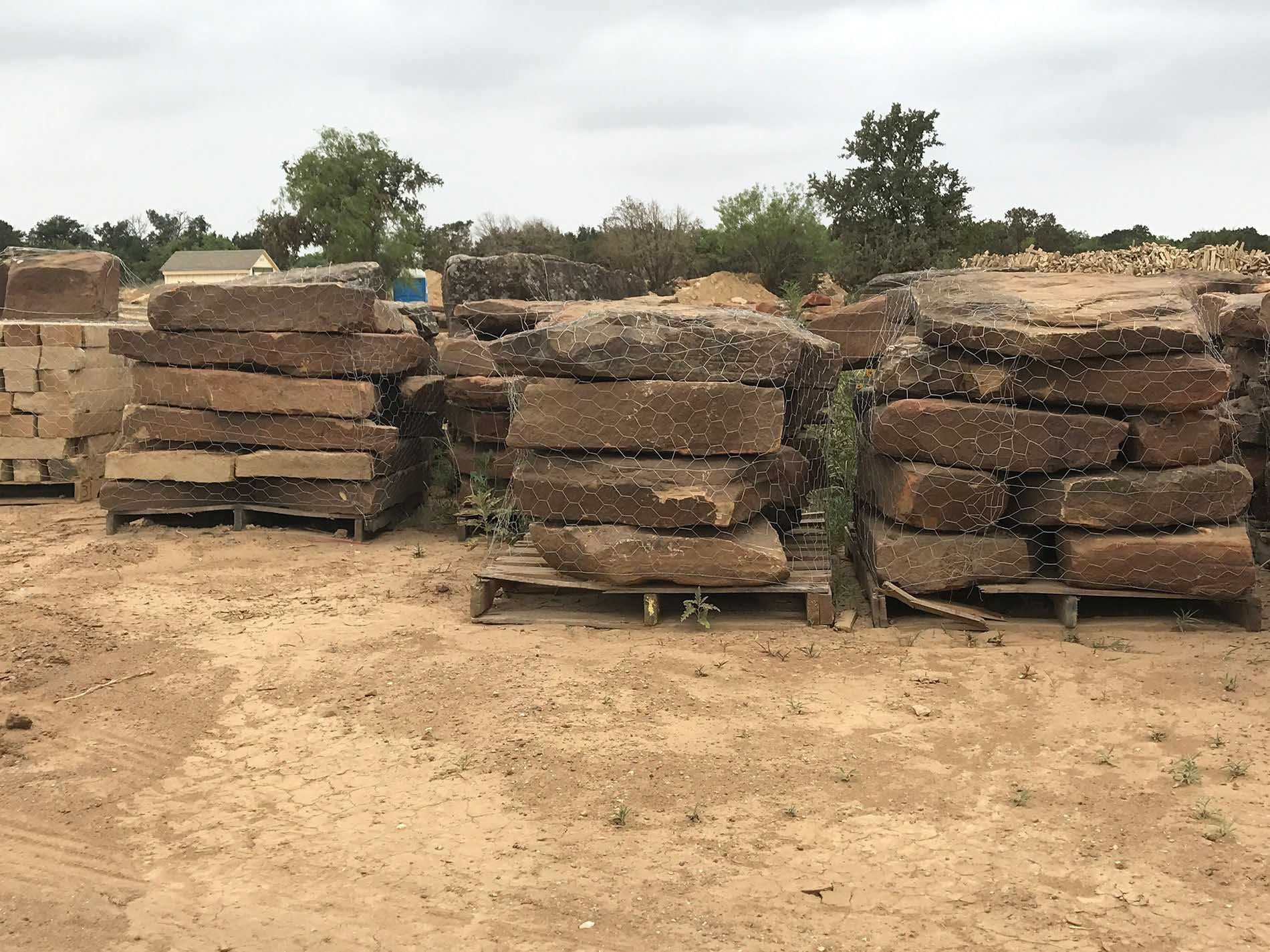 Piles of rectangular, rough-hewn stone slabs on wooden pallets in an outdoor setting.
