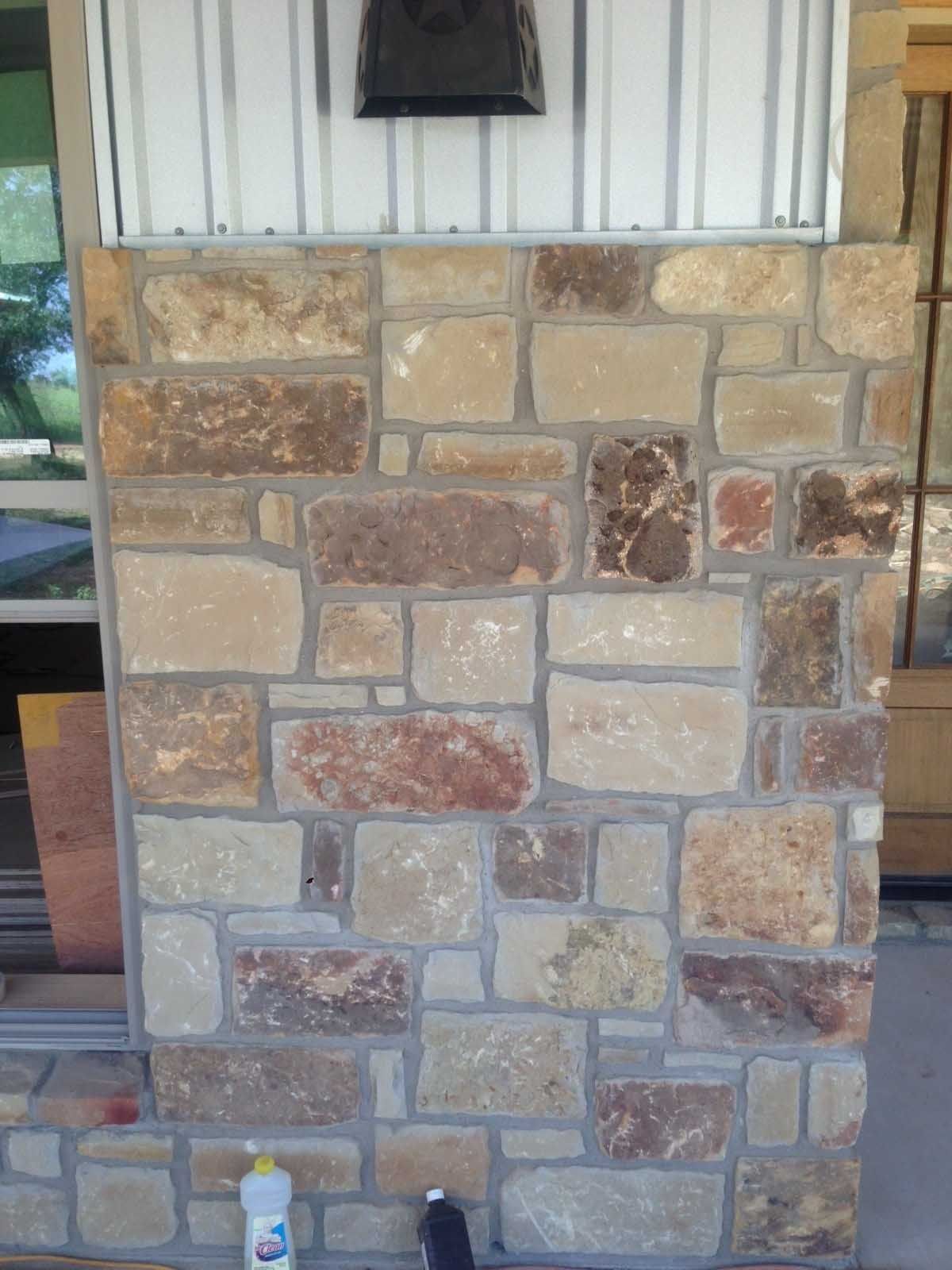 Stone wall with varying shades of tan, brown, and red, below a metal panel and a black object.