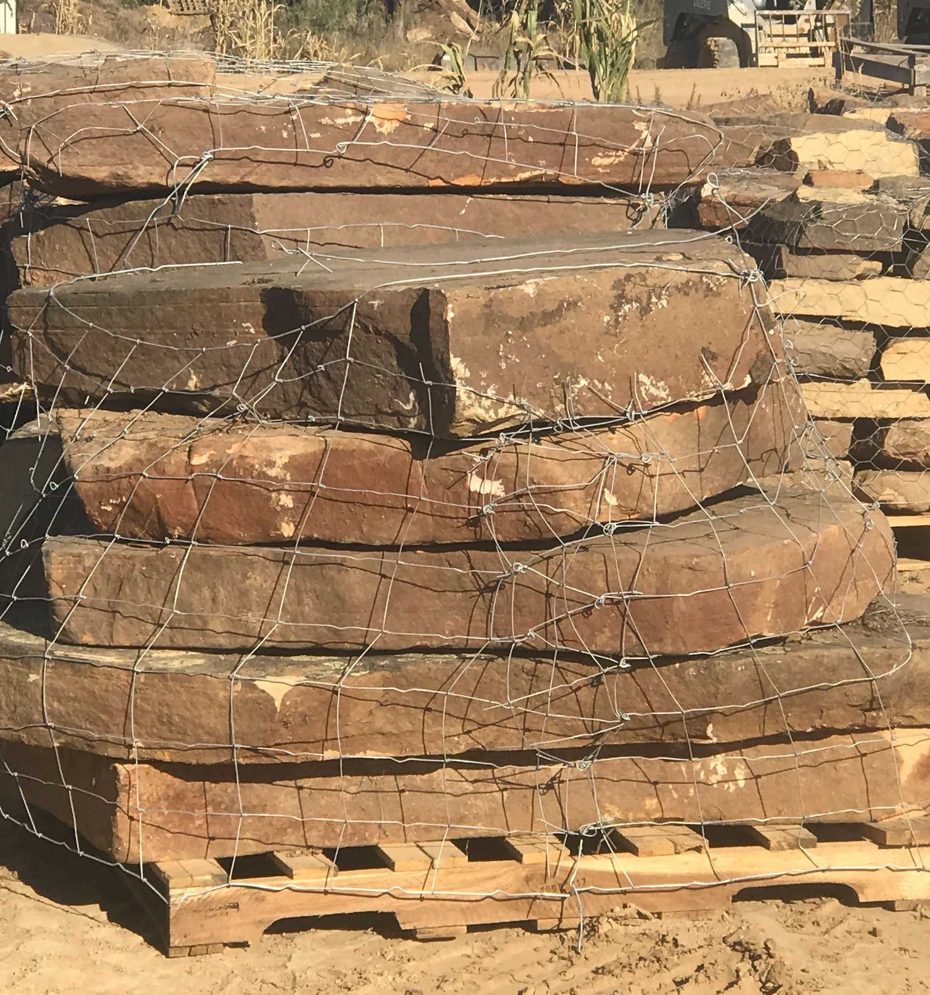 Stack of reddish-brown, irregularly shaped stones secured with wire mesh on a wooden pallet.
