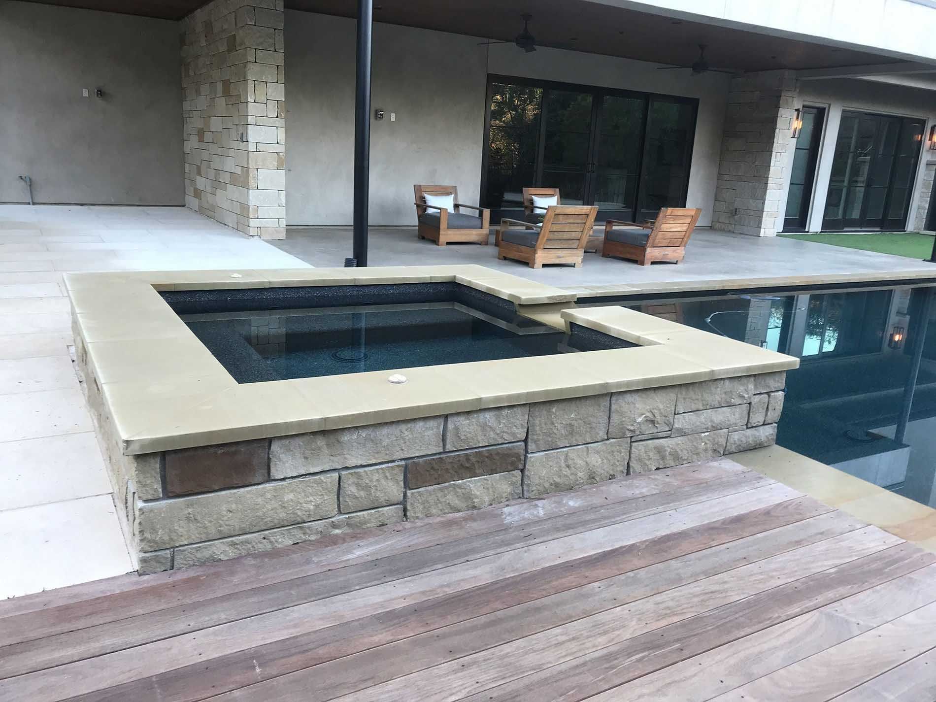 Hot tub and pool with stone surround and wooden deck, part of an outdoor patio setting.