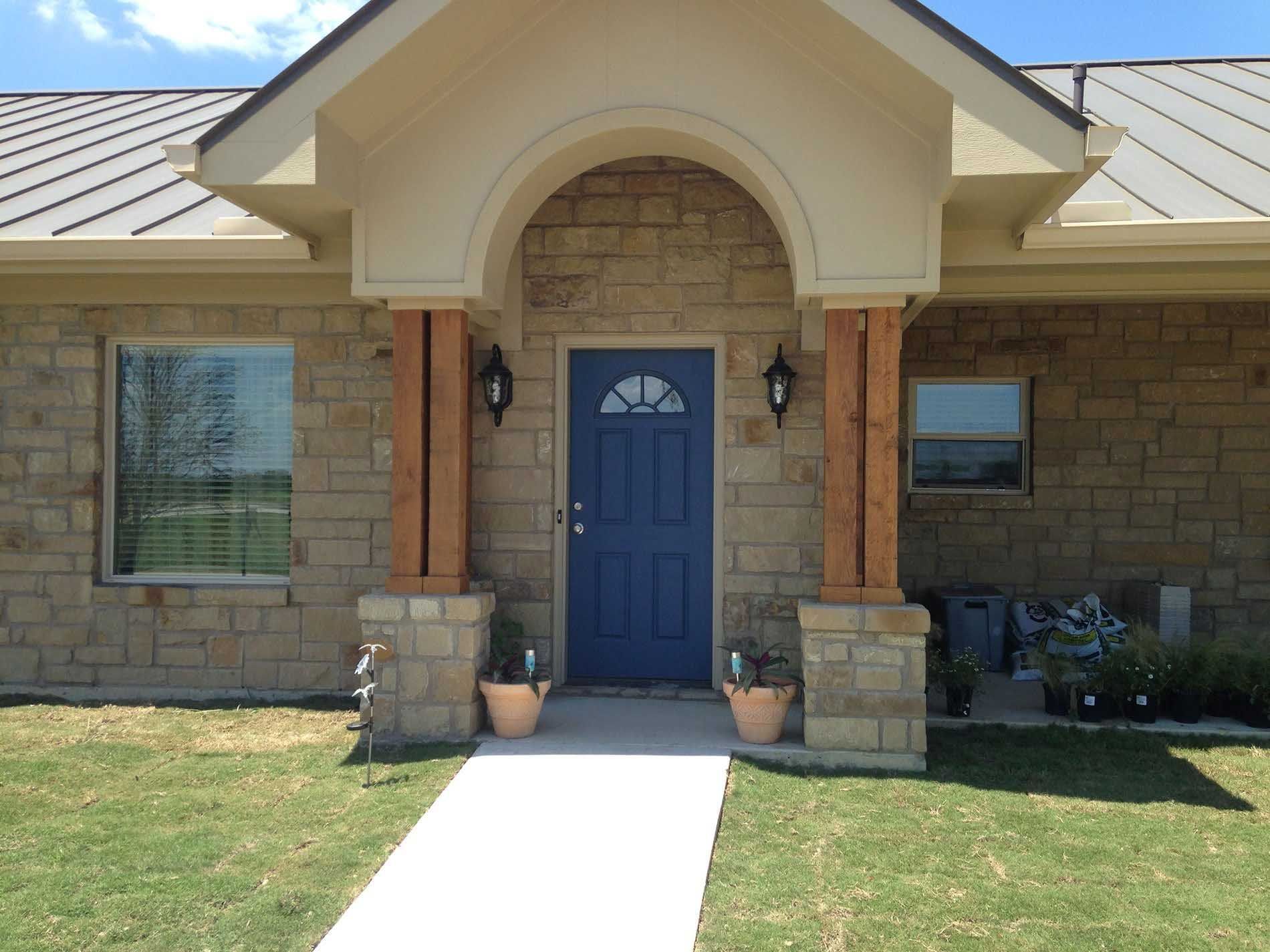 Blue front door with stone facade, under a tan archway supported by wood pillars.