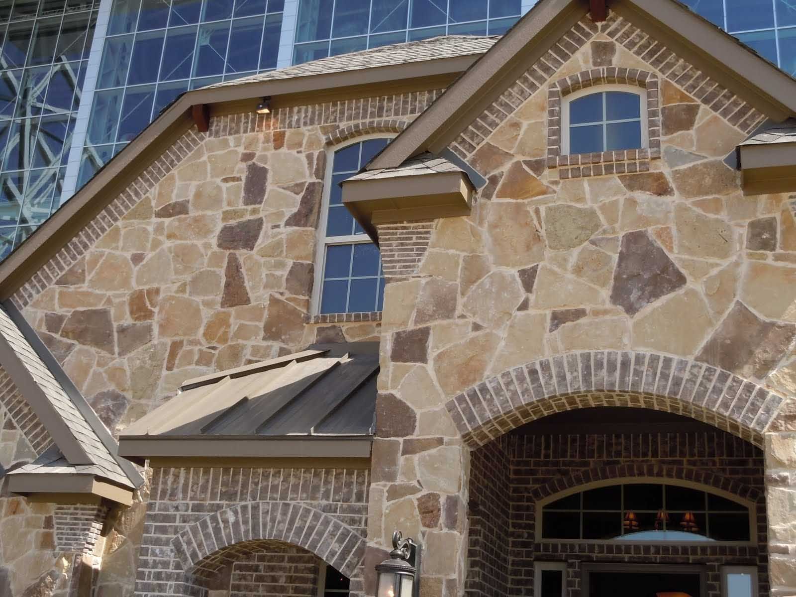 Stone exterior of a house with arched brick entryway and small windows.