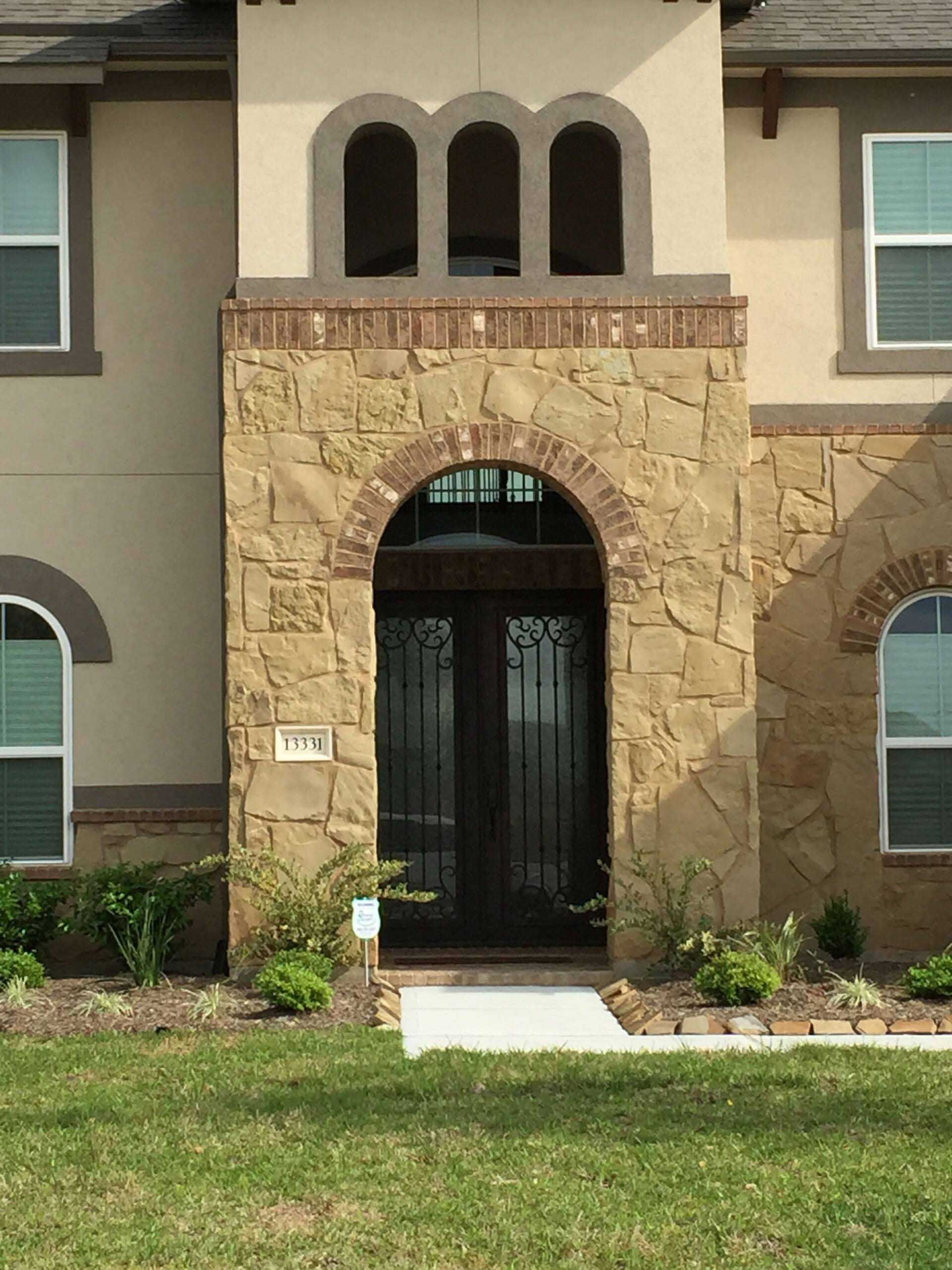 Stone-covered entryway with arched door and upper arches in a two-story beige house.