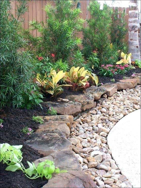 Stone-edged garden bed with mulch, colorful plants, and decorative rocks bordering a curved concrete path.