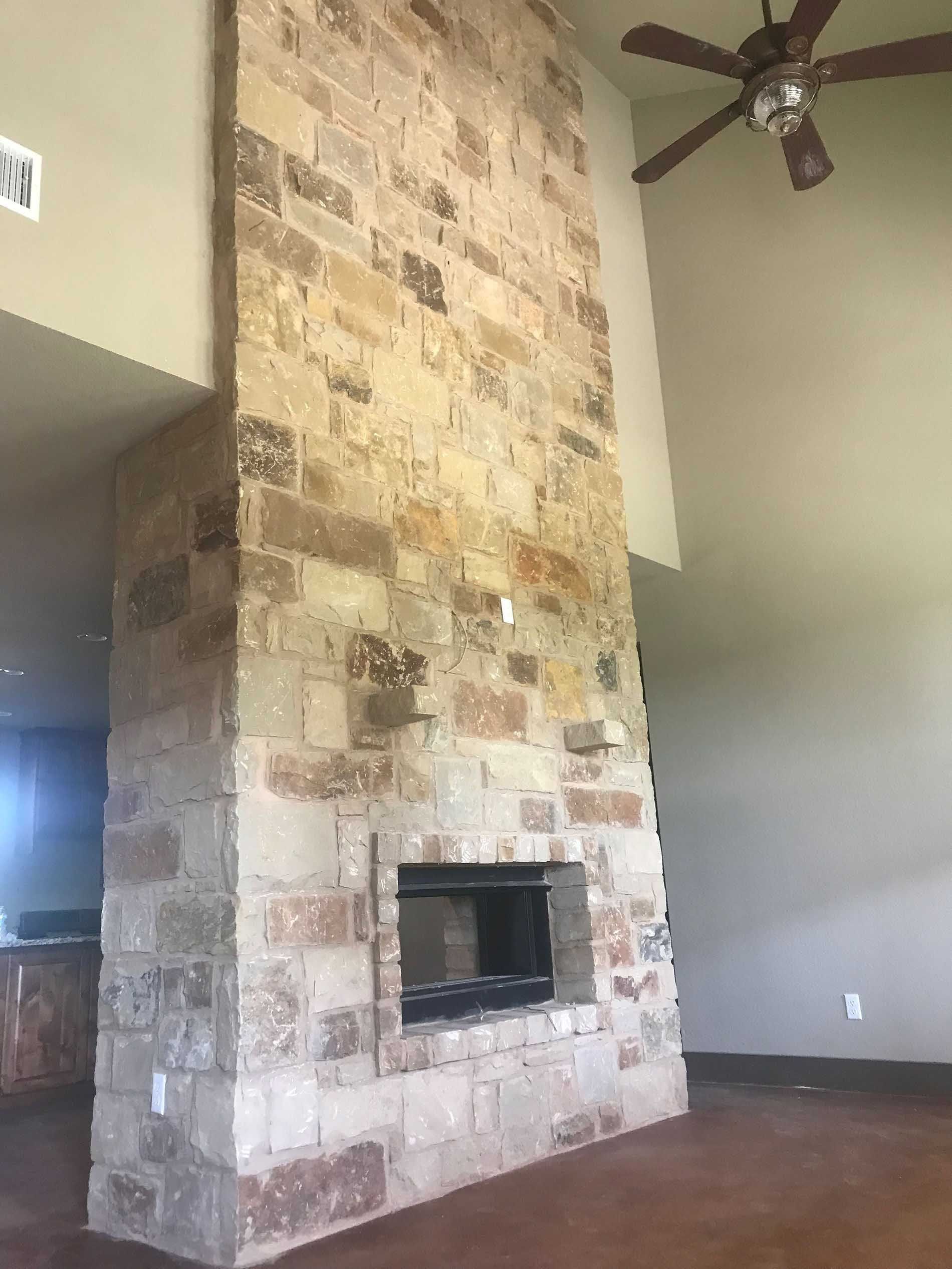 Tall stone fireplace with rectangular opening, reaching to vaulted ceiling. Brown ceiling fan.