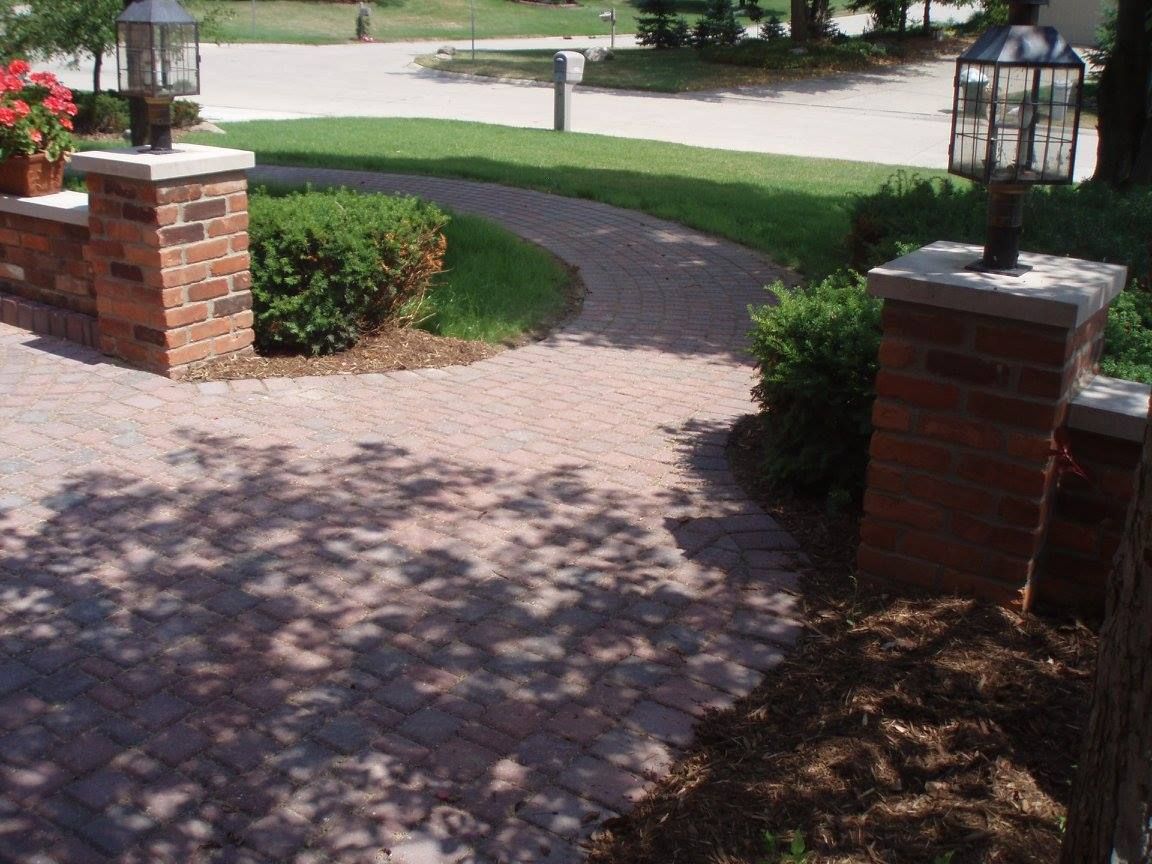 Circular brick patio under construction next to a lawn, featuring assembled bricks and others in a row ready for placement.