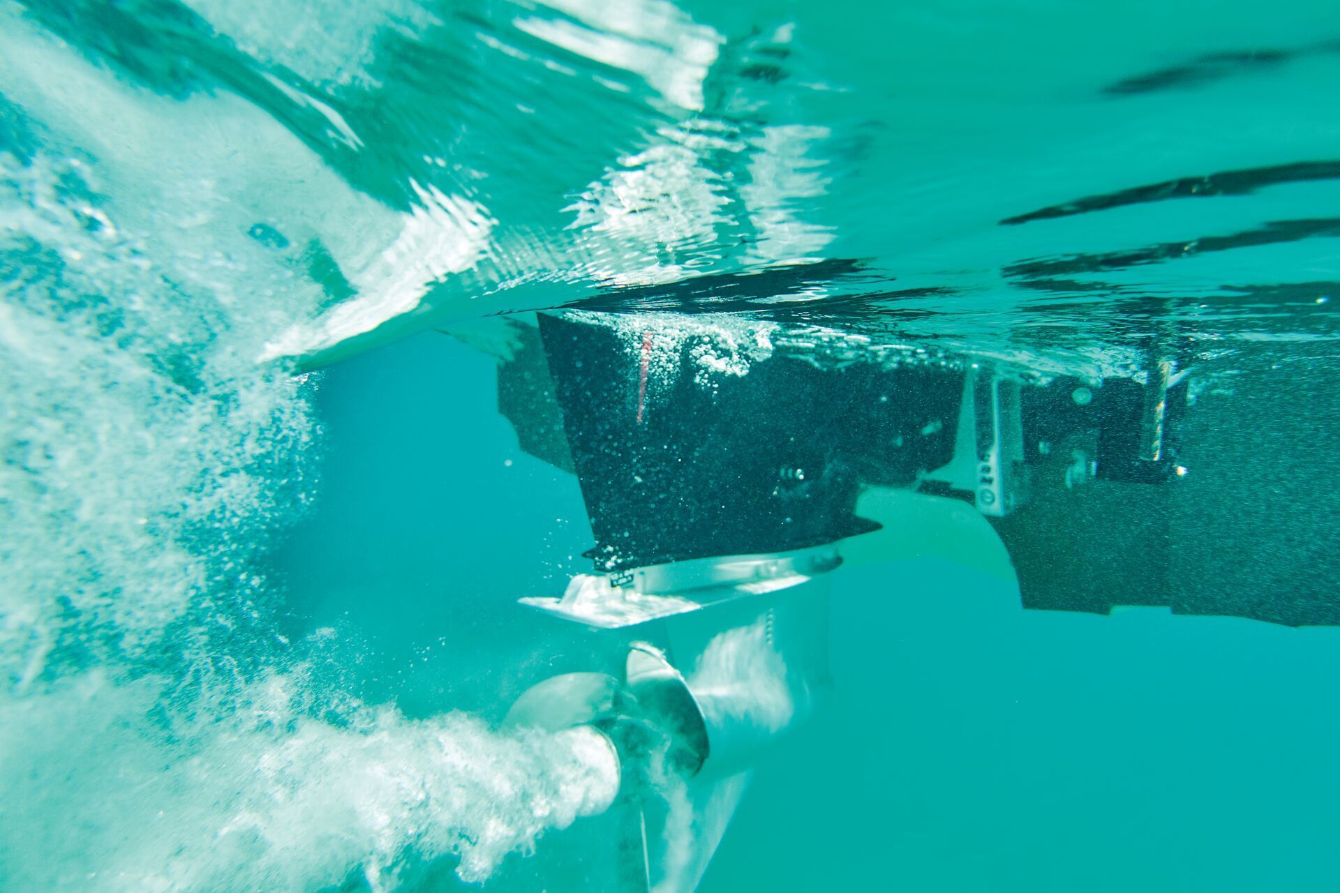 Underwater view of a boat motor propeller churning water and creating bubbles in clear turquoise water.