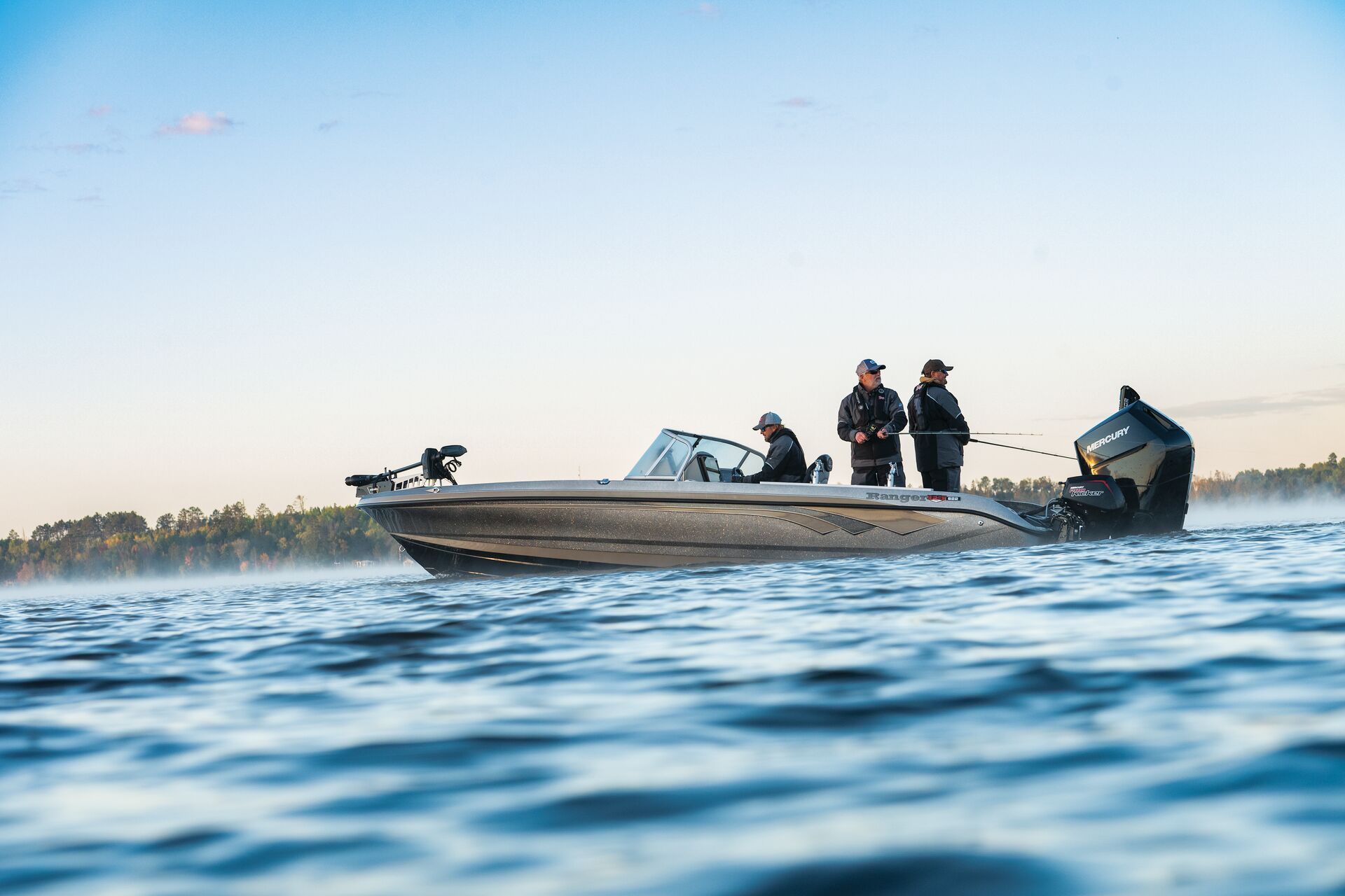 Three people fish from a boat on calm, misty water under a clear blue sky.